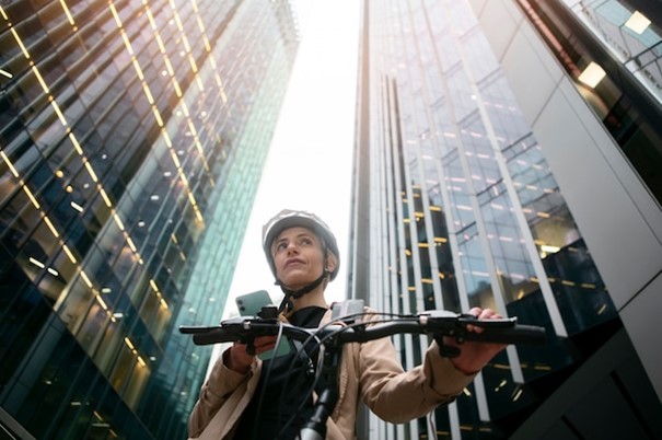 Free photo woman holding her smartphone and walking by her bike